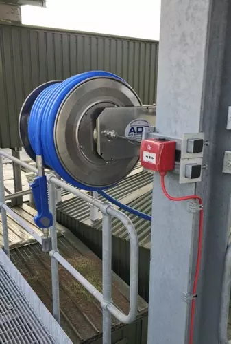 Outdoor medium-pressure stainless steel hose reel with blue hose mounted to a steel structure at an industrial washdown site in Burton.